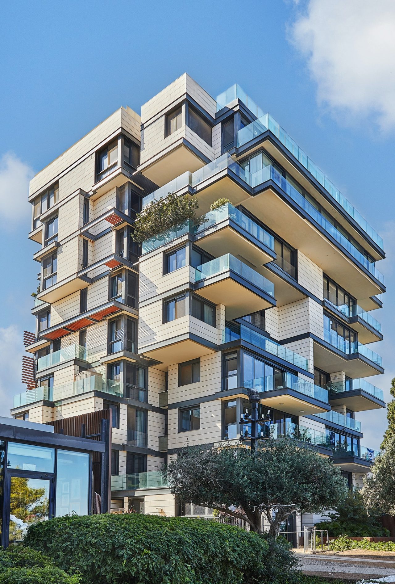 Modern multi-storey apartment building with glass balconies and contemporary architectural design under clear blue sky